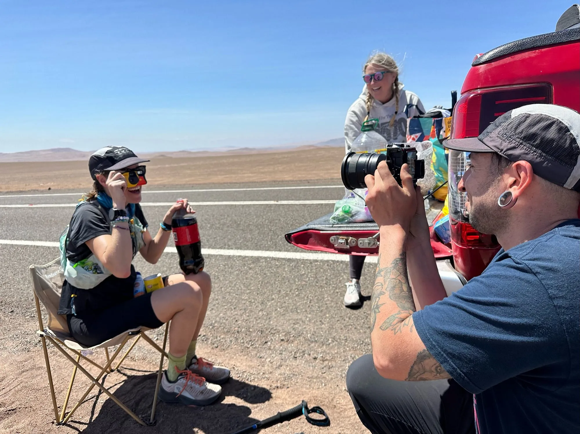 Lucy sitting in a camp chair at a roadside crew stop in the Atacama while a crew member photographs her.