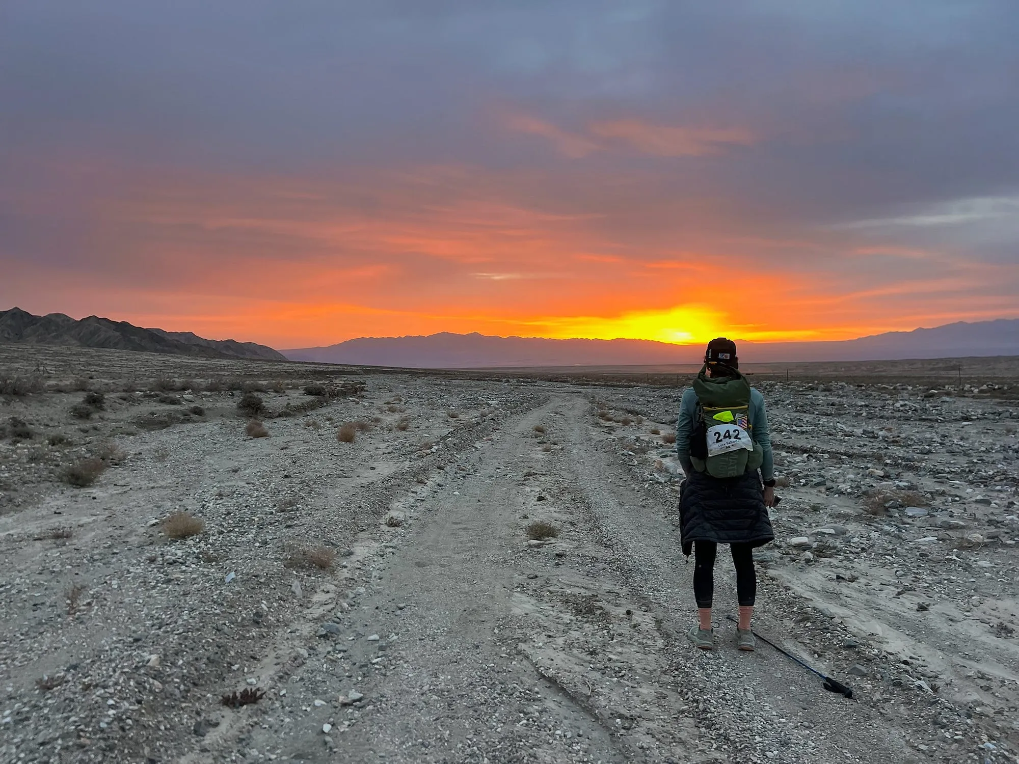 Sunrise over the Gobi desert with a lone runner on a dirt double-track in the distance.