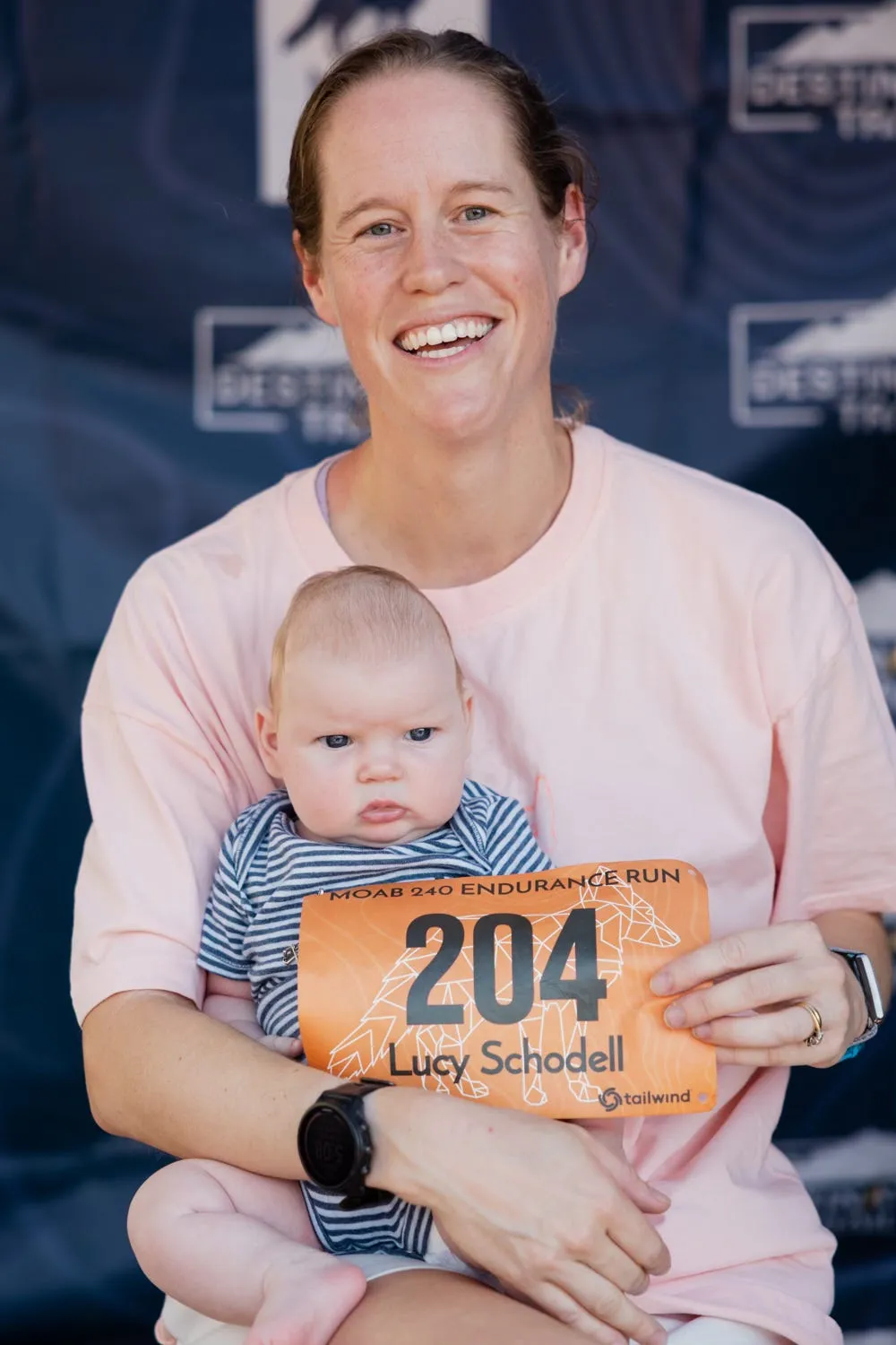 Lucy at the Moab 240 start holding her infant daughter, who is holding race bib number 204.