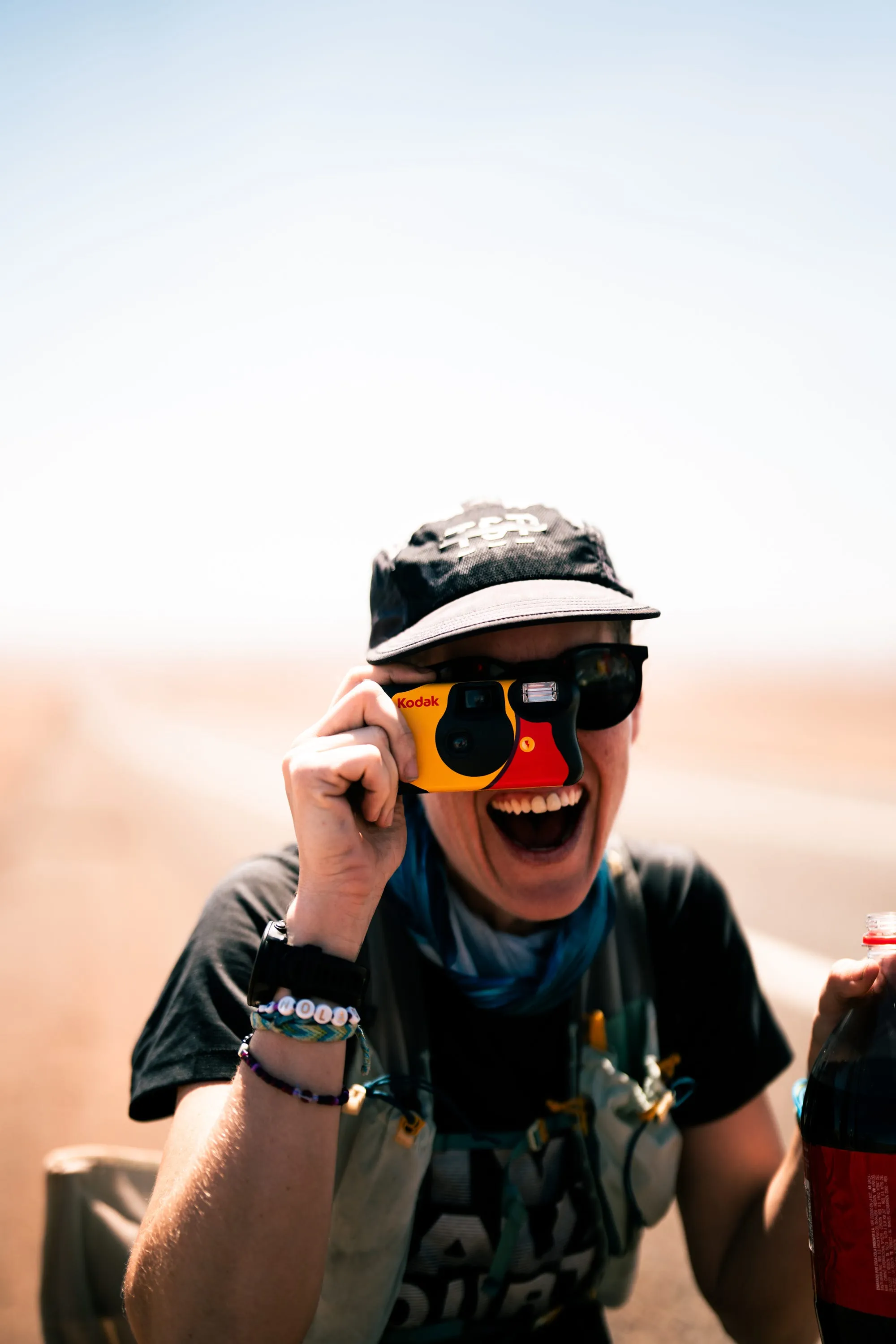 Lucy laughing mid-race in a cap and orange sunglasses, hand raised to her visor.