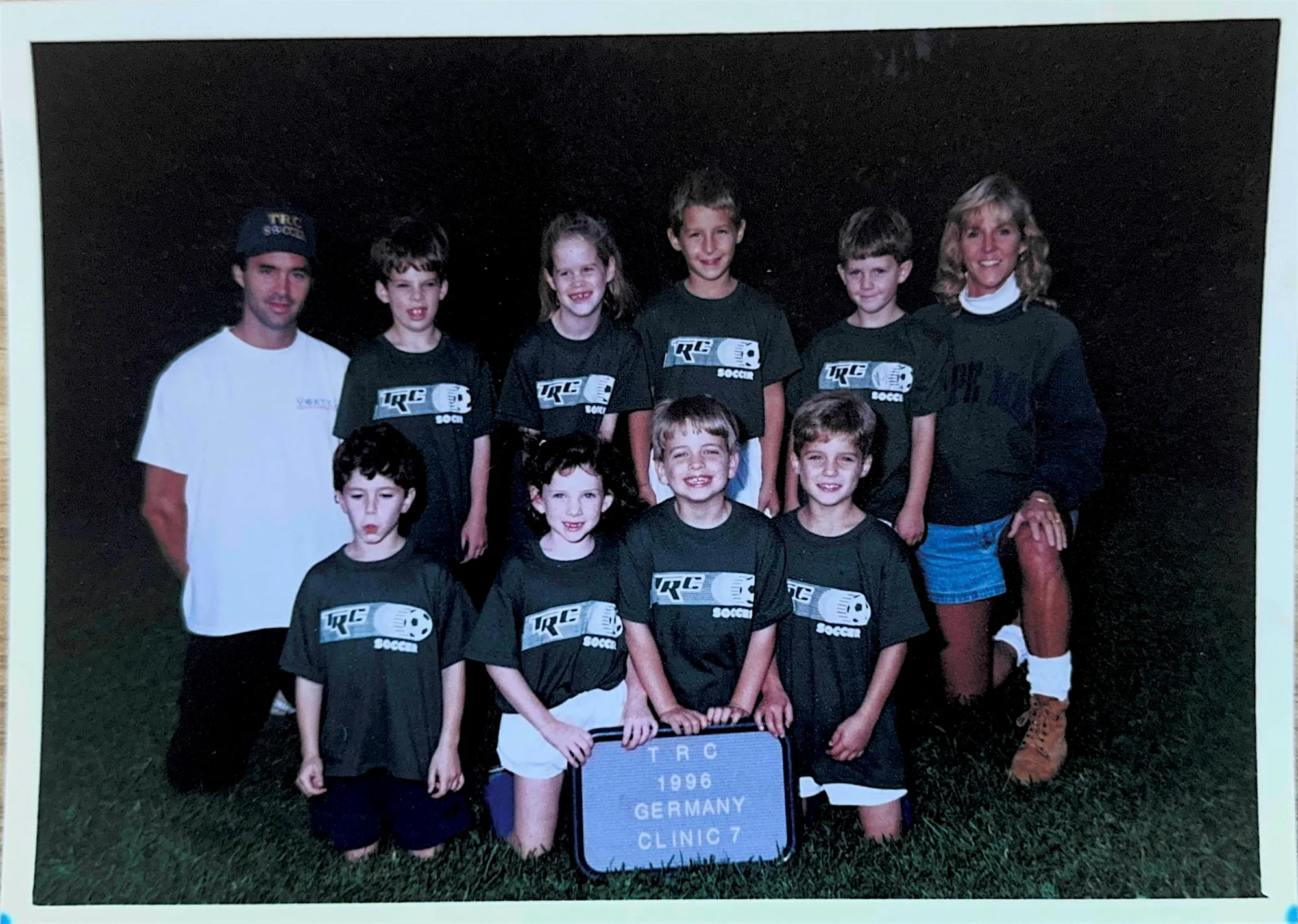An old print photograph of a youth sports clinic team posed on a grass field with their coach.