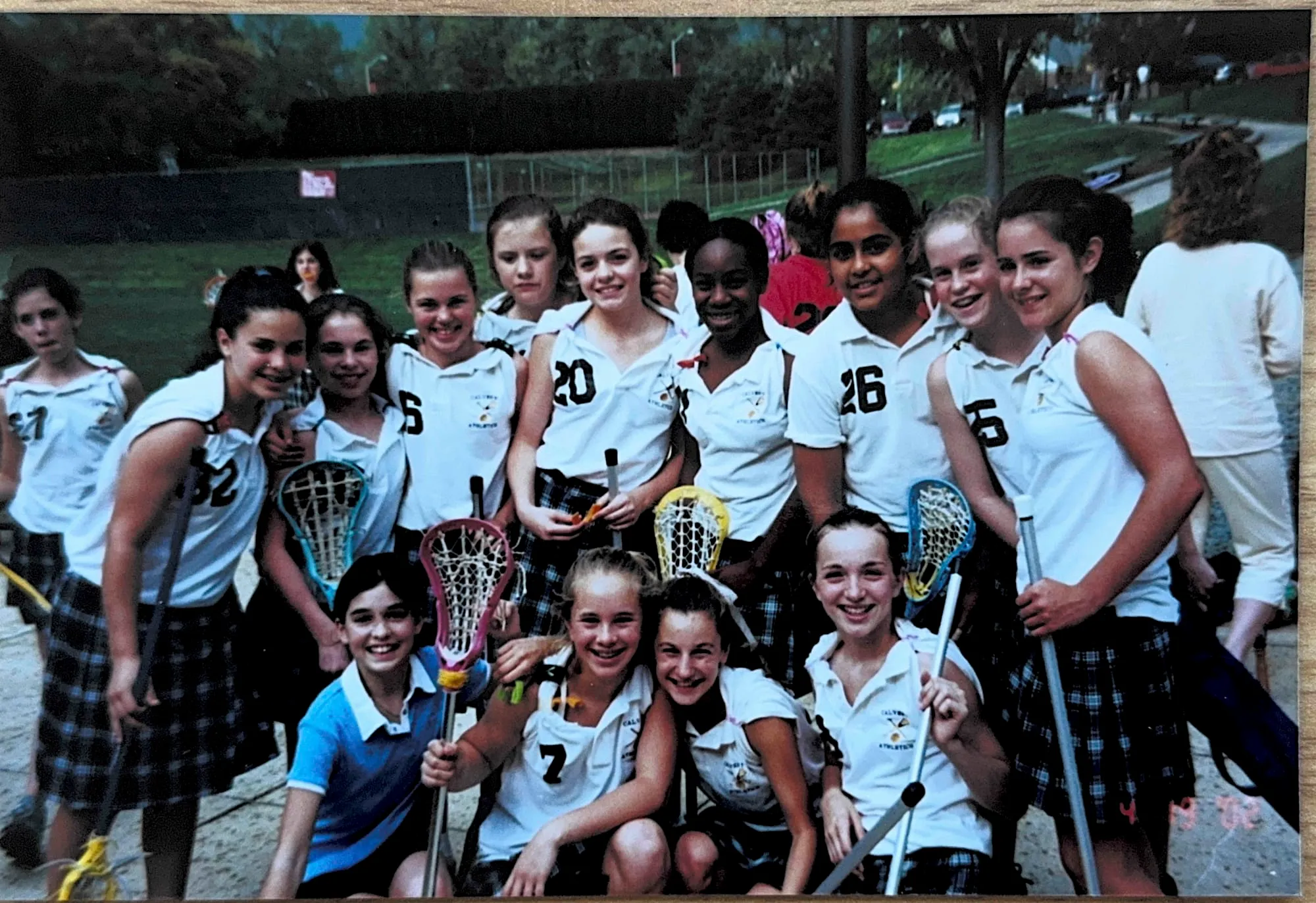 A youth girls' lacrosse team photo, players in white kit holding sticks.